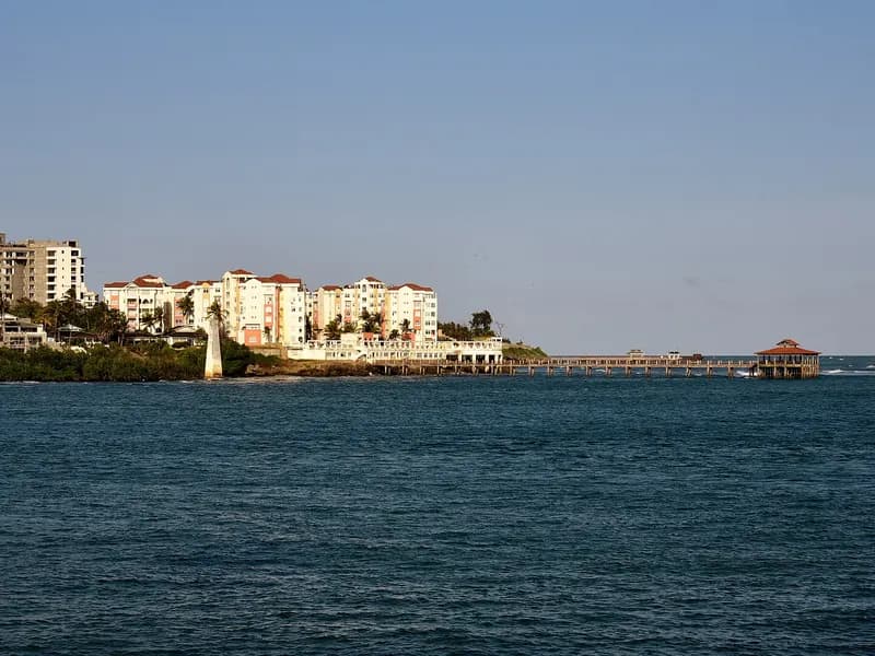 Multi-storey apartment buildings and a wooden pier along a coastal shoreline under clear skies