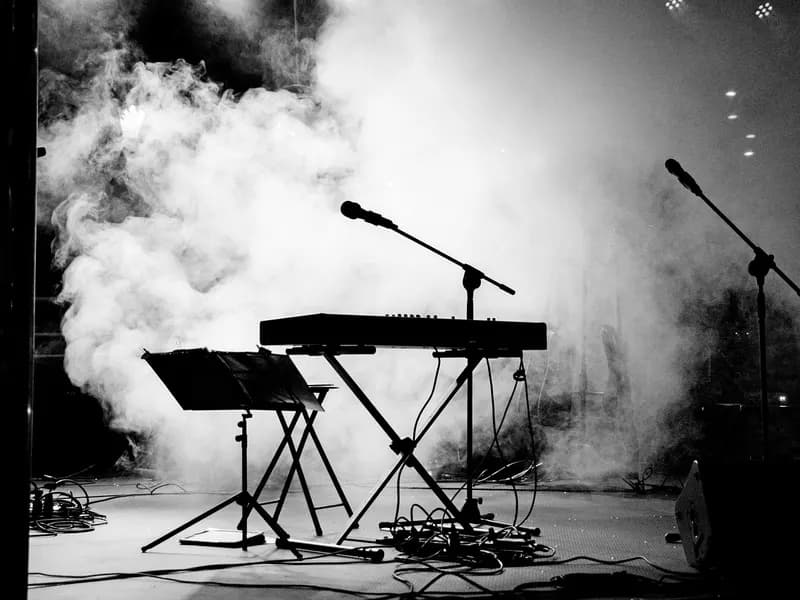 Black and white stage with keyboard, microphone stands, and smoke during a concert