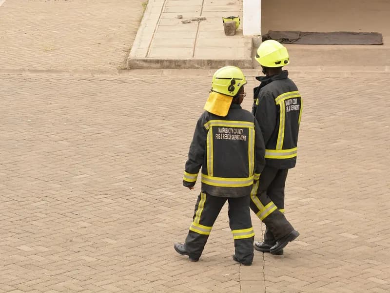 Two firefighters in Nairobi City County Fire & Rescue uniforms walking across a brick plaza