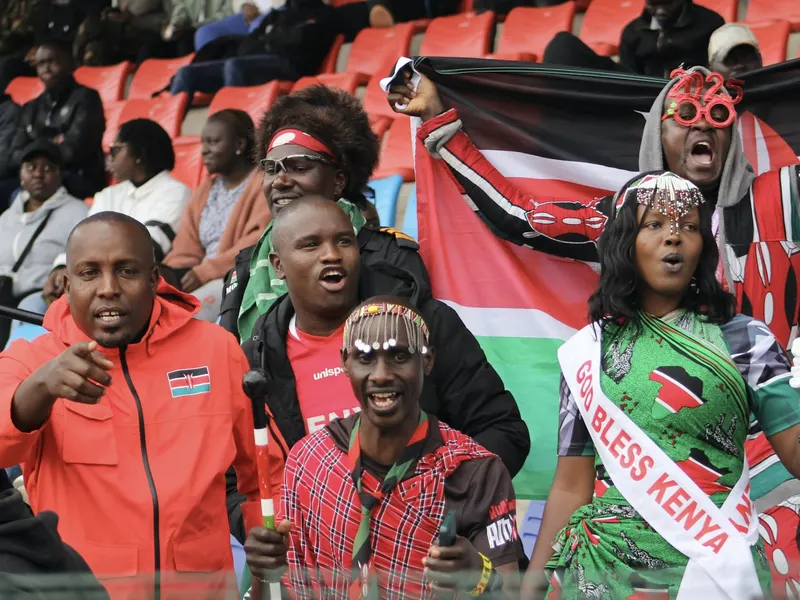 Kenyan fans in a stadium stand waving the Kenyan flag and cheering