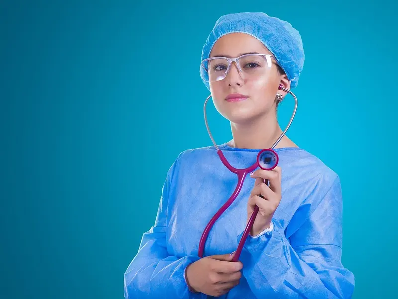Young woman in blue scrubs and cap holding a red stethoscope against a teal background